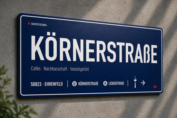 Aluminium-Designtafel „Körnerstraße“ von DasIstColonia mit weißem Rahmen an einer Betonwand. Design Straßenschild für Köln-Liebhaber