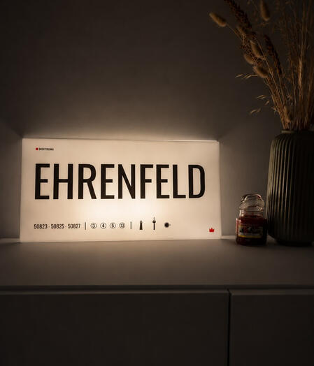 Detailaufnahme des Designschilds „Ehrenfeld“ Acrylglas-Designschild „Ehrenfeld“ von DasIstColonia in einer modernen Wohnumgebung mit warmer Beleuchtung. Design Straßenschild für Köln-Liebhaber