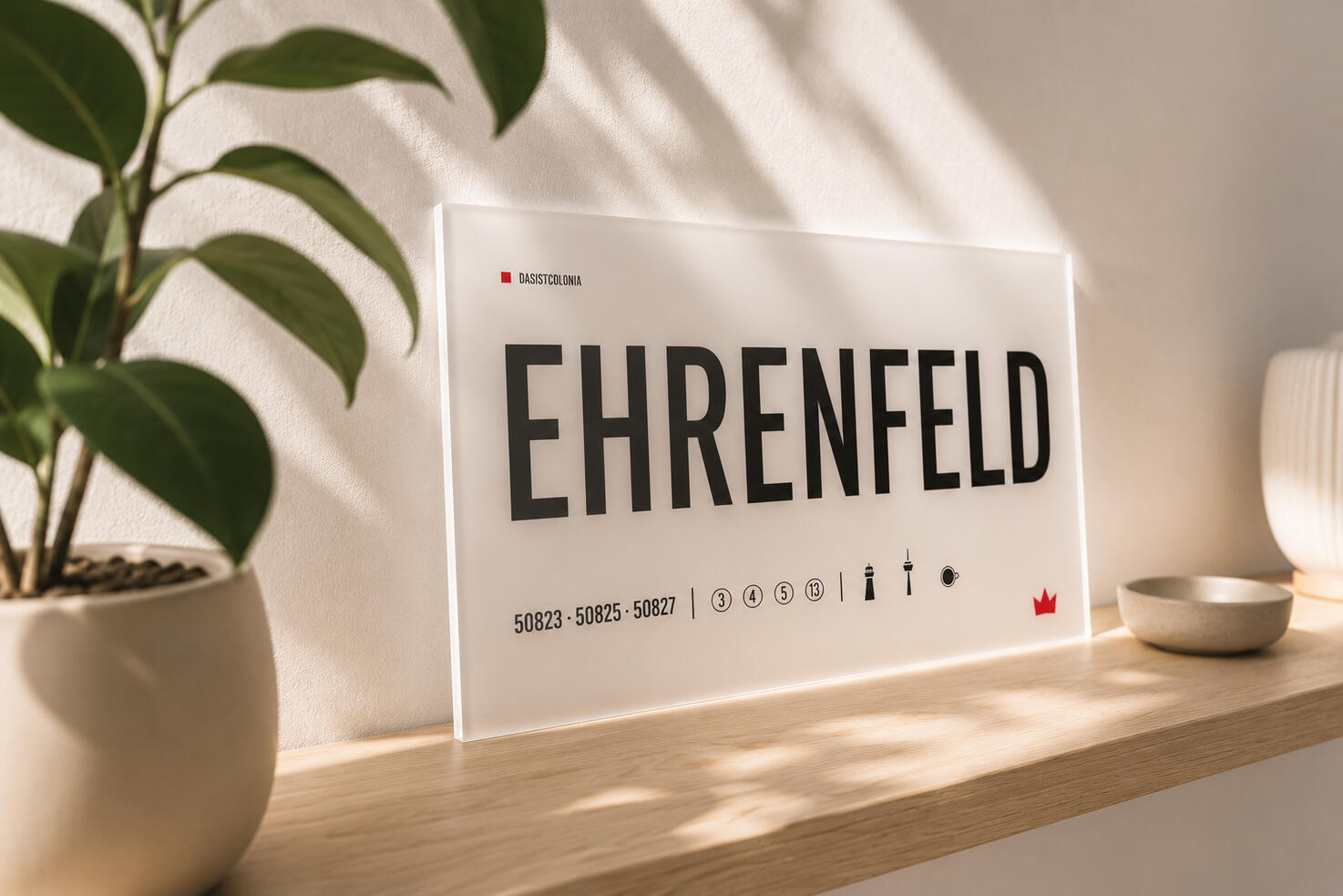 Ehrenfeld Designschild aus opalem Acrylglas „Ehrenfeld“ von DasIstColonia auf einem hellen Regal im warmen Tageslicht. Design Straßenschild für Köln-Liebhaber